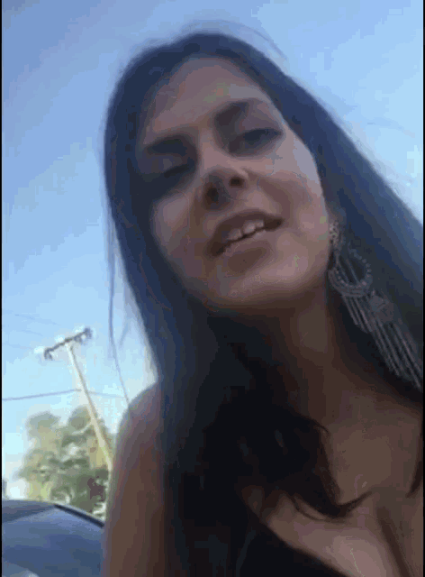 a woman wearing a black top and earrings looks at the camera