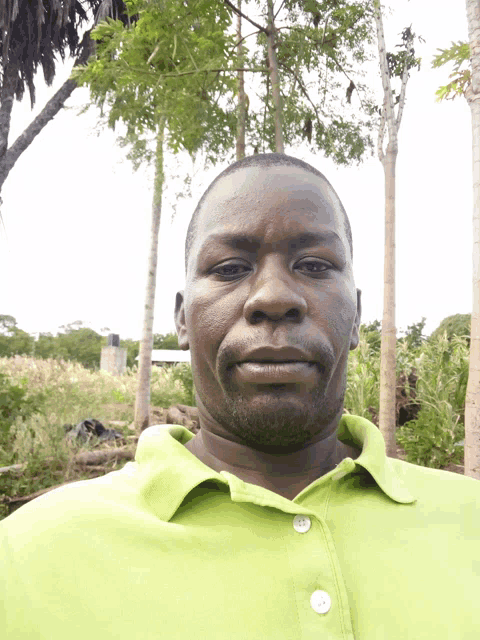 a man wearing a green shirt is standing in front of trees