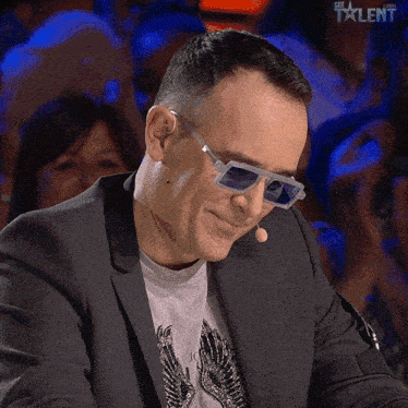a man wearing sunglasses and a suit is sitting in front of a microphone with the word talent on the screen behind him