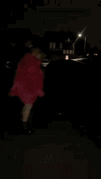 a woman in a pink coat is dancing in the dark .