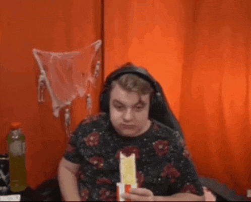 a man wearing headphones is eating a sandwich in front of an orange curtain