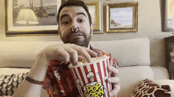 a man sitting on a couch eating popcorn from a striped bucket