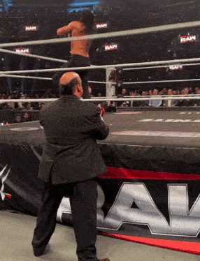 a man in a suit stands in a wrestling ring with a sign that says raw