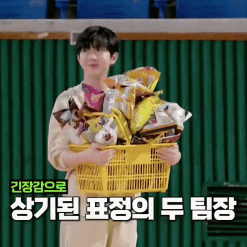 a boy is holding a basket full of snacks with korean writing behind him