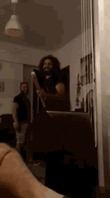 a man with long hair is standing in a living room holding a sword .