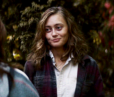 a woman wearing a plaid shirt and a necklace looks at the camera