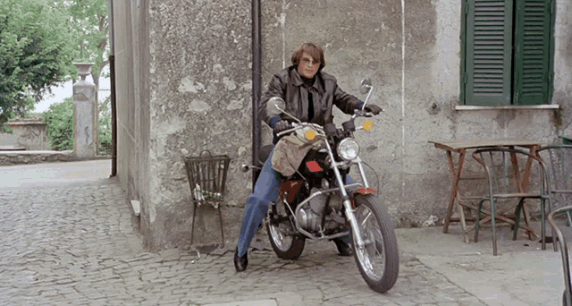 a man in a leather jacket is riding a motorcycle on a cobblestone street
