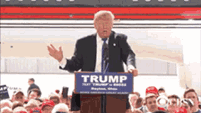 a man stands at a podium holding a sign that says trump