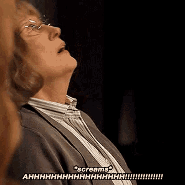 a woman wearing glasses is screaming in a dark room while looking up .