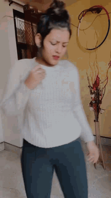 a woman in a white sweater is dancing in a room