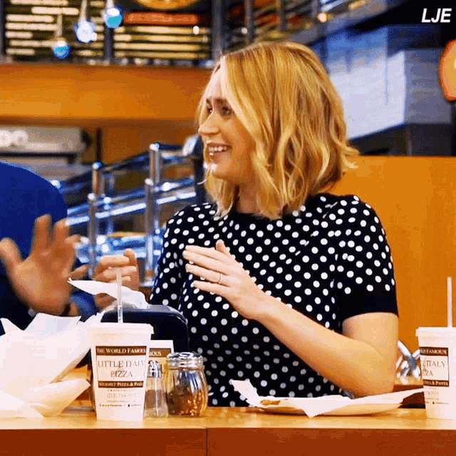 a woman sitting at a table with a cup that says little italia pizza on it