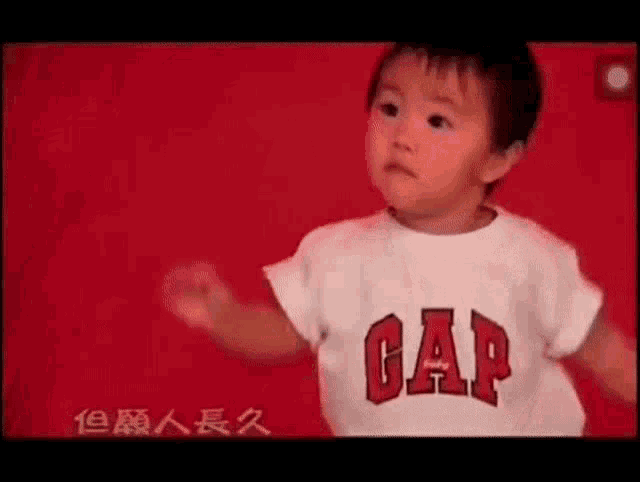 a little boy wearing a gap t-shirt is standing on a red background .