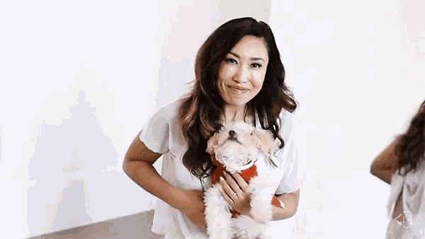 a woman in a white shirt is holding a small white dog in her arms