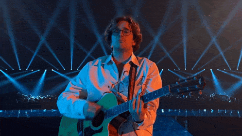 a man wearing glasses is playing a guitar on a stage