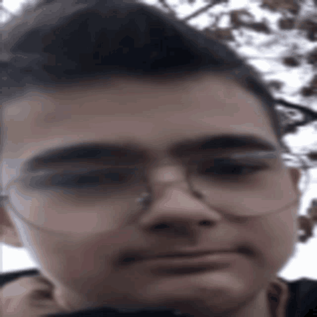 a young man wearing glasses looks at the camera with a serious look on his face