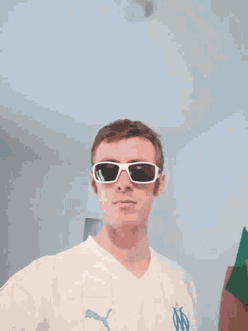 a man wearing sunglasses and a white shirt with the letter m on it