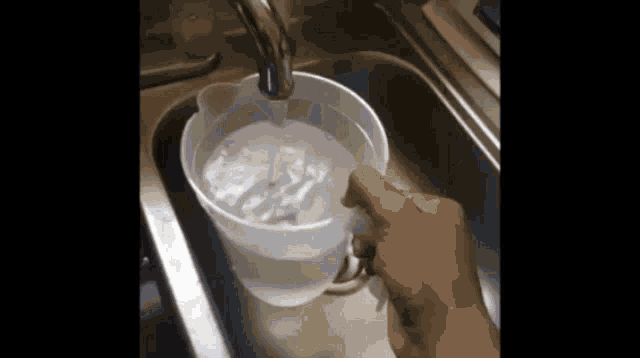 a person is pouring water into a pitcher in a kitchen sink