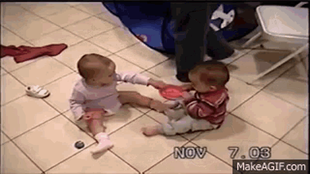 two babies are sitting on a tiled floor playing with toys .