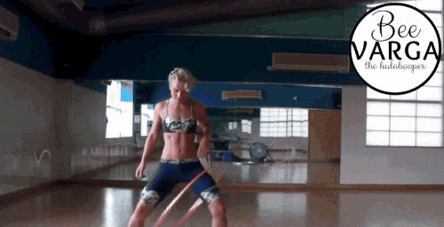 a woman is doing hula hooping in a gym with a bee varga logo behind her
