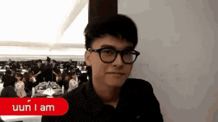 a young man wearing glasses is standing in front of a crowd and says i am