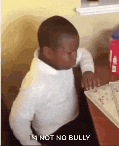 a young boy is sitting at a desk with his eyes closed and the words im not no bully above him .