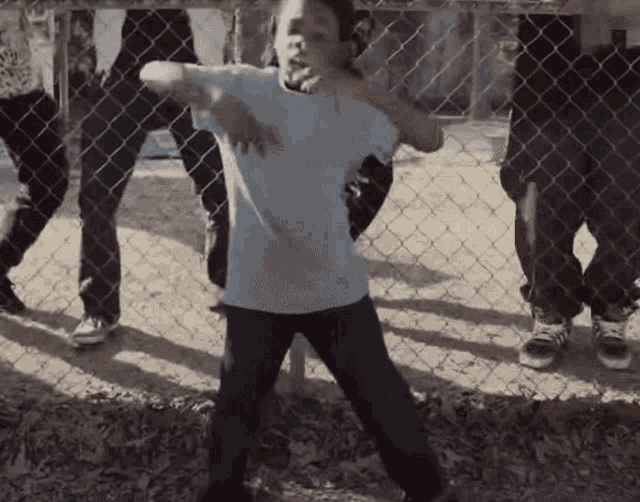 a young boy stands in front of a chain link fence with his arms outstretched