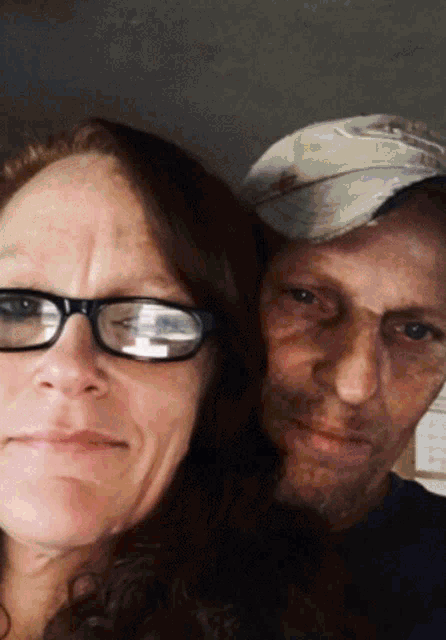 a woman wearing glasses is standing next to a man wearing a hat