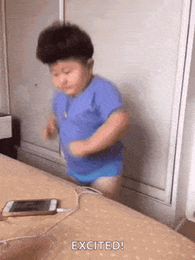 a little boy in a blue shirt is jumping on a bed next to a phone .