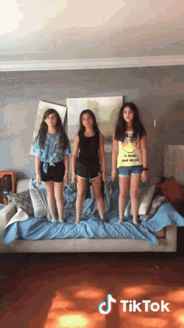three girls standing on top of a couch with a tiktok logo on the bottom