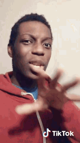 a young man in a red hoodie is making a funny face with a tiktok watermark on the bottom right