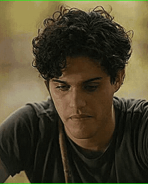 a man with curly hair is wearing a black shirt and looking down .