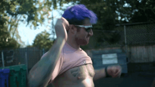 a man with purple hair and a tattoo on his chest takes off his shirt