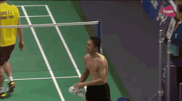 a man without a shirt is standing on a badminton court