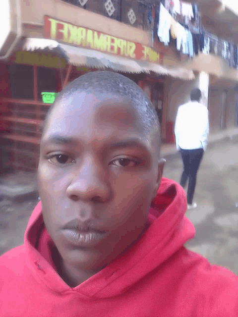a man wearing a red hoodie stands in front of a building with a sign that says " t " on it