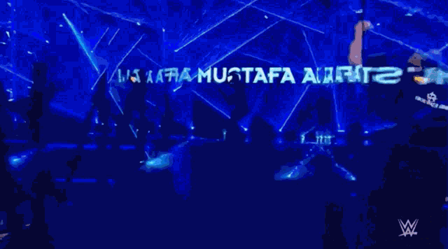 a wrestler is standing in front of a sign that says ' mustafa ali '