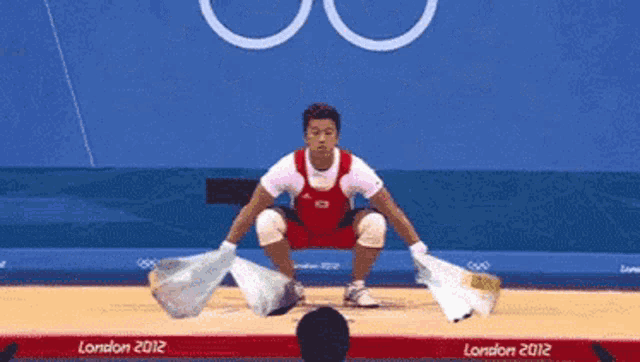 a man squatting on a wrestling mat in front of a sign that says london 2012