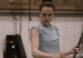 a woman in a blue shirt is standing in a room holding a sword .