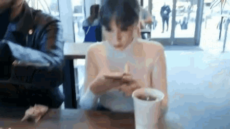 a woman is sitting at a table with a cup of coffee and looking at her cell phone .