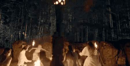 a group of people are dancing around a fire in a dark forest .