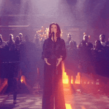 a woman singing into a microphone while a choir stands behind her