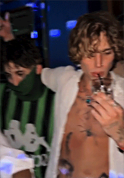 a shirtless man in a kappa shirt drinks from a straw