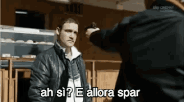 a man in a leather jacket is pointing a gun at another man in a store .