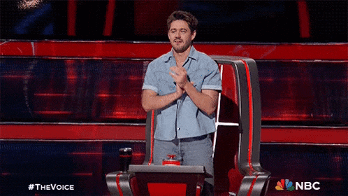 a man is sitting in a chair on a stage with his hands folded .