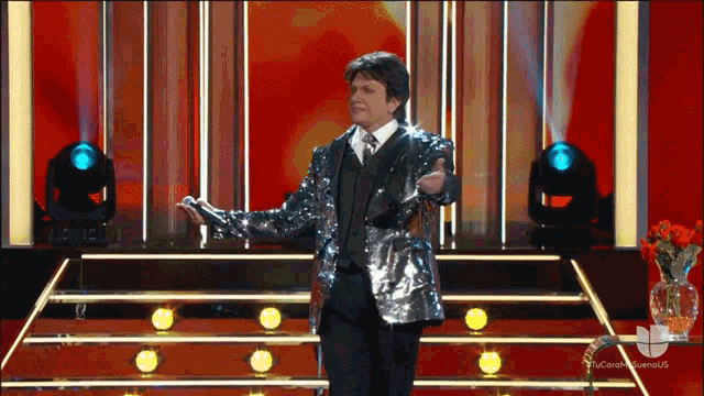 a man in a sequined suit stands on a stage with a microphone