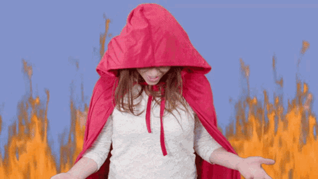 a woman in a red cape is screaming in front of a fire background