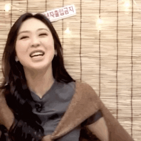 a woman in a brown sweater is laughing in front of a bamboo curtain .