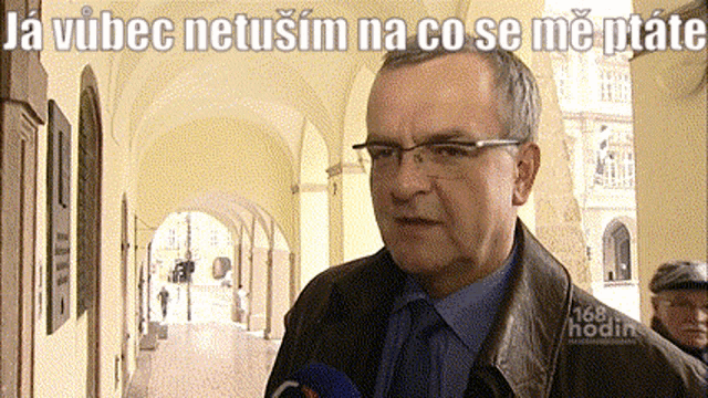 a man wearing glasses stands in front of a sign that says ja vucec netusim na co se me ptate