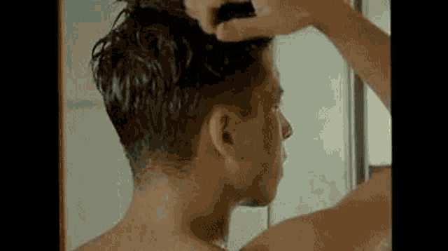 a man is brushing his hair in front of a mirror in a bathroom .