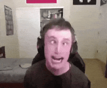 a man is wearing headphones and making a funny face in a bedroom .