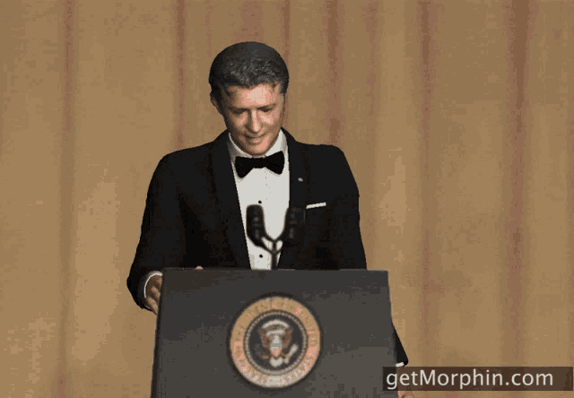 a man in a tuxedo is giving a speech at a podium that says getmorphin.com